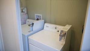 Une buanderie équipée de deux lave-linge et deux sèche-linge Whirlpool blancs, d’une petite étagère avec une boîte et d’un mur orné d’un motif.