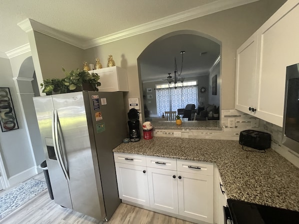 A modern kitchen with white cabinets, a stainless steel refrigerator, a coffee maker, and a toaster on the countertop.