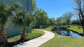 A landscaped area with a curved pathway, a small pond, and a wooden bridge. - Myrtle Beach Resort Unit 5110 - Ideal Beach Getaway (Myrtle Beach)