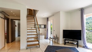 En moderne stue med en trætrappe, et fladskærms-tv, en sofa og udsigt til en balkon med et bjergpanorama.