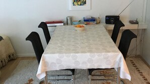 Een eetgedeelte met een tafel, stoelen, een radio en een schilderij aan de muur.