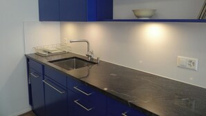 Een moderne keuken met een zwart aanrecht, een roestvrijstalen spoelbak en blauwe keukenkastjes.