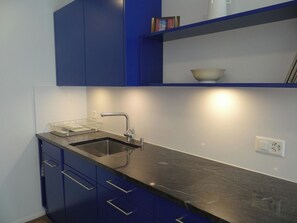 Eine moderne Küche mit schwarzer Arbeitsplatte, einer Edelstahl-Spüle und blauen Schränken.