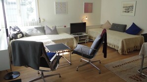 A modern room with a bed, a desk with a laptop, a chair, a TV, and artwork on the walls.