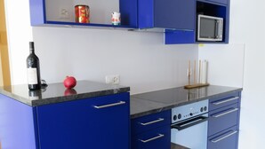 Een keuken met blauwe kastjes, een magnetron, een fornuis en een wijnfles.