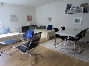 Una sala de estar moderna con un sofá, una mesa de centro, una mesa de comedor con sillas, un televisor y una estantería.