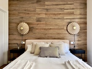 A bedroom with a wooden wall, two bedside tables, a bed with multiple pillows, and two wall-mounted lamps. - Housingleón - Muralla II (León)