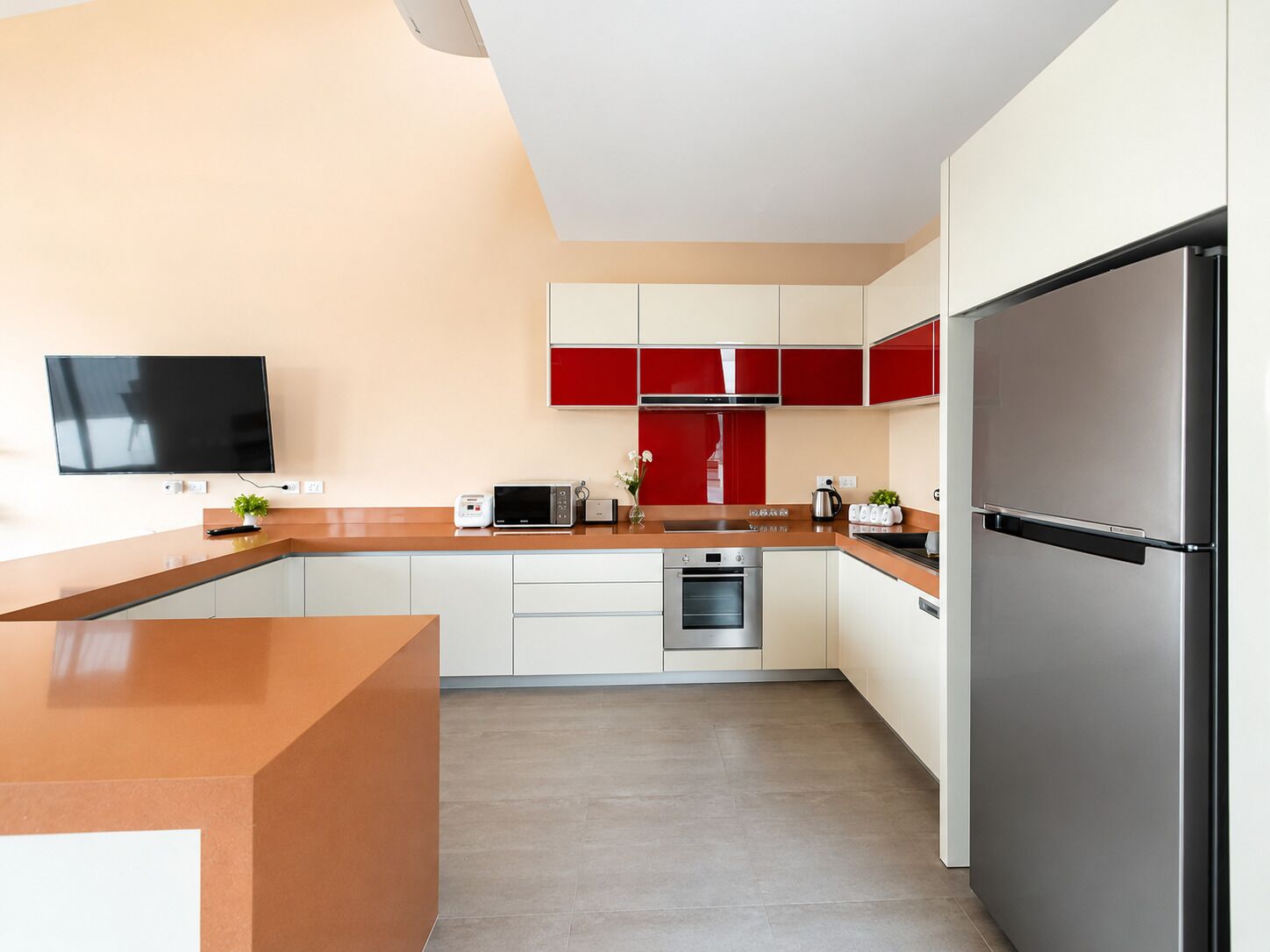 Una cucina moderna con schermo piatto, forno a microonde, tostapane, frigorifero e forno integrato.
