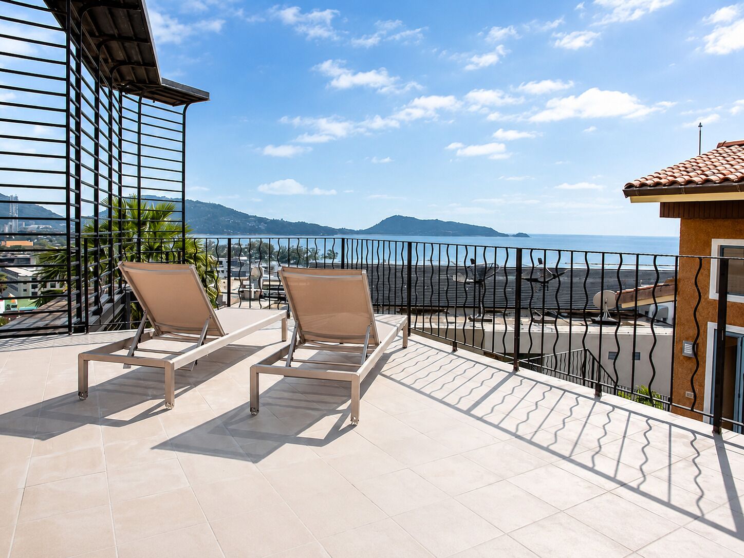 A balcony with two sun loungers, a metal railing, and a view of the sea and mountains.