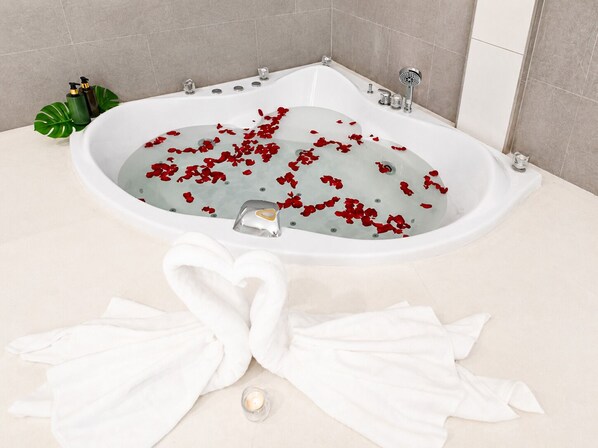 A bathtub with rose petals, a white towel, and a candle. - Teetara Villa Patong (Patong)