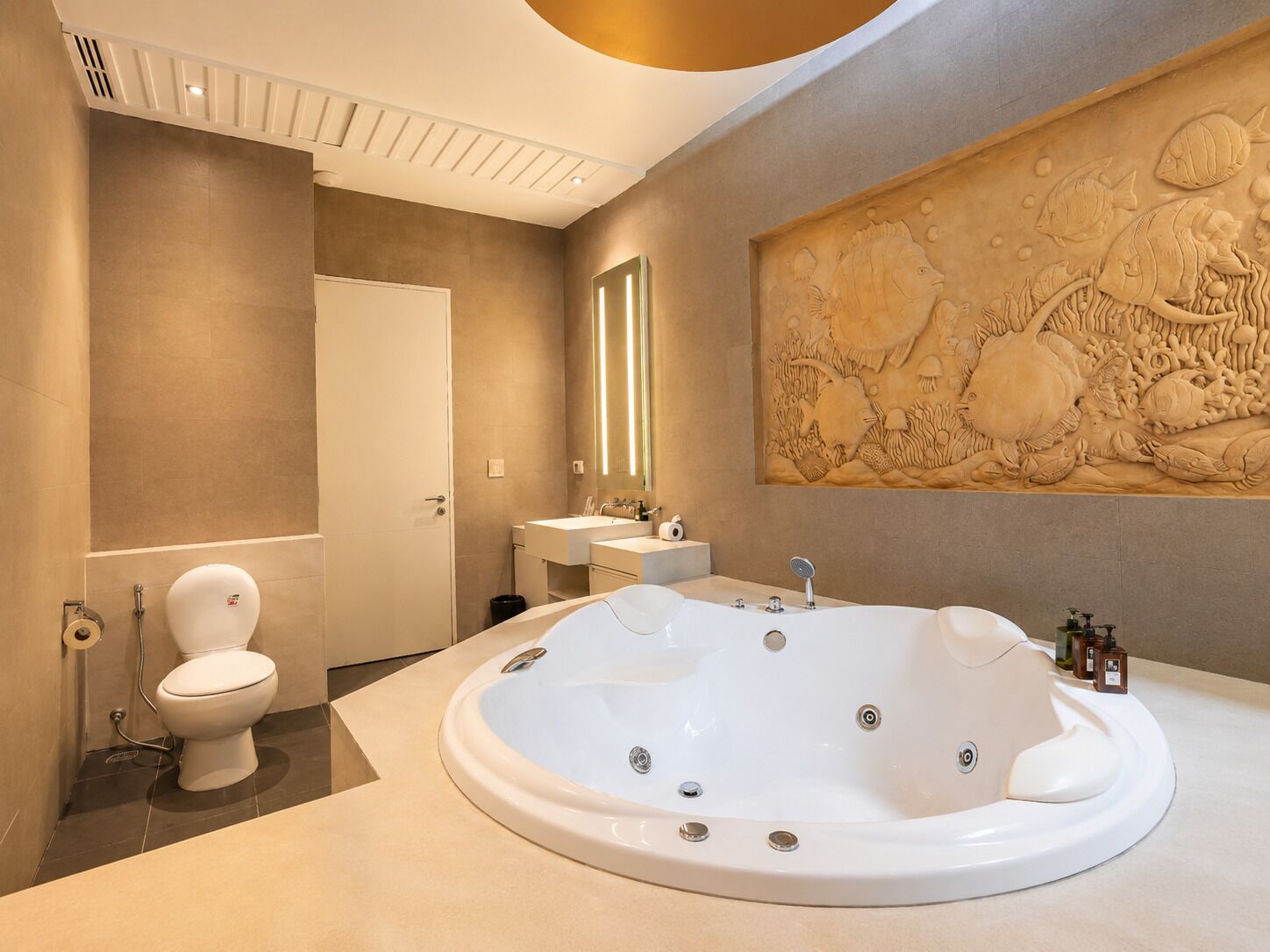 Une salle de bain moderne avec une grande baignoire sur pieds, des toilettes, un lavabo et un décor mural sculpté.