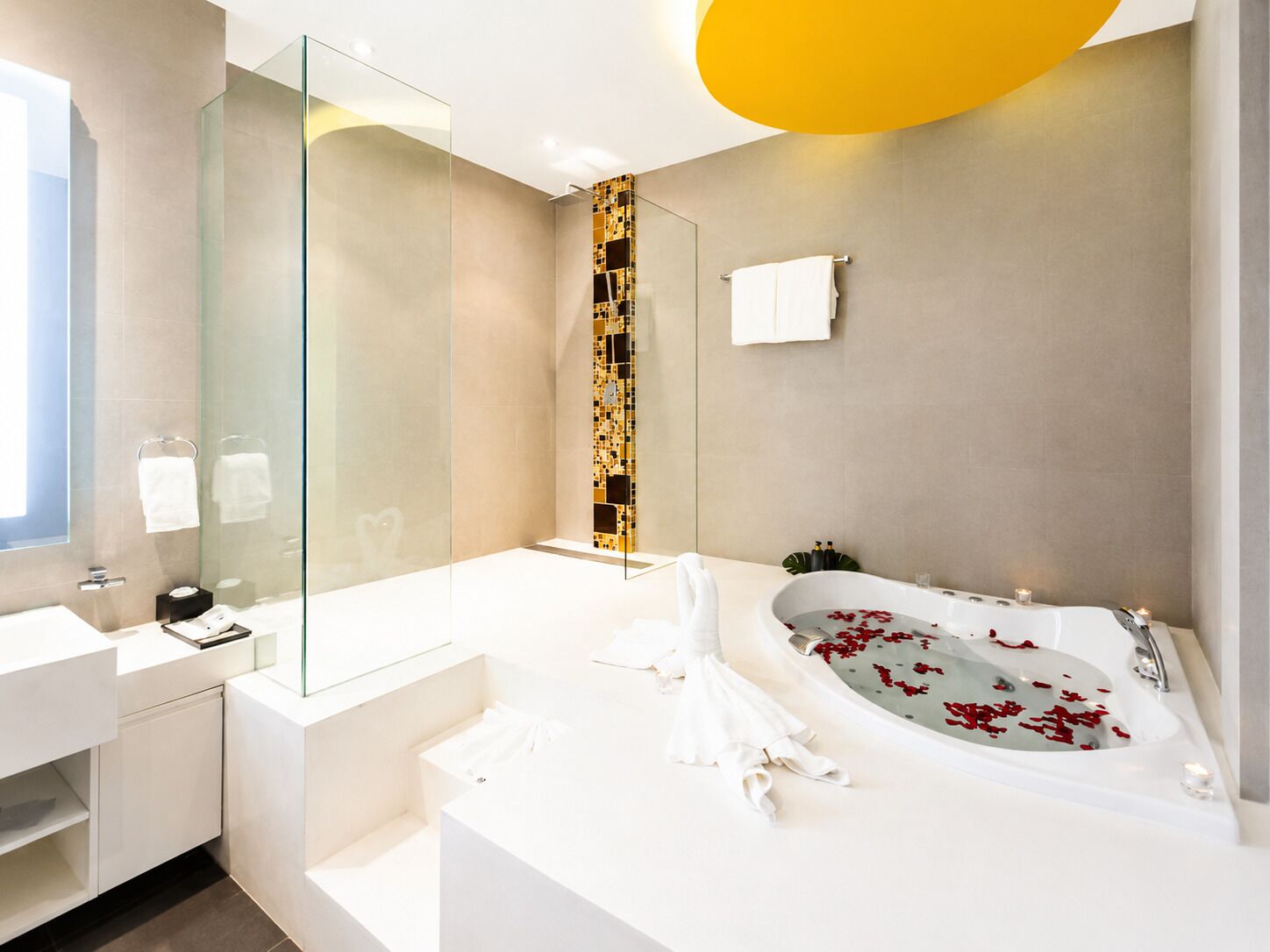 Une salle de bain moderne avec une douche à parois de verre, une baignoire remplie de pétales de roses et un grand miroir.