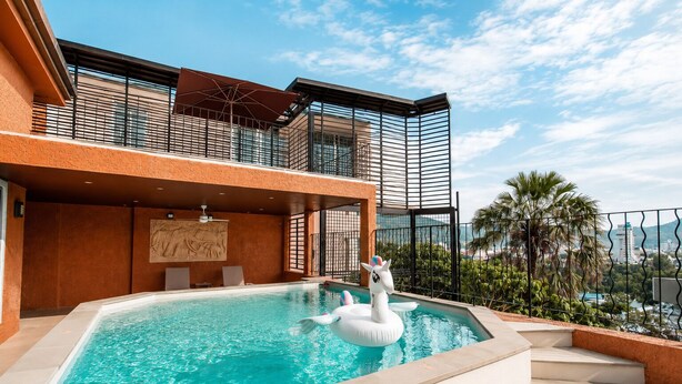 A swimming pool with a swan float, a mural, and a view of the cityscape. - Teetara Villa Patong (Patong)
