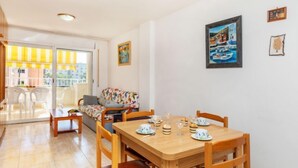 En matplats med ett träbord för fyra personer, en soffa och en balkong med vita stolar.