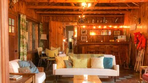 Interior acogedor de una cabaña de madera con sofá, sillones, una mesa de centro y una zona de bar con un letrero de 'No Fumar'.