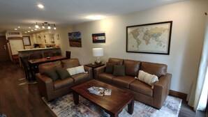 A living room with a brown leather sofa, a wooden coffee table, and a world map on the wall. - Perfect location off 4 o'clock run, Walk to Mainstreet, Ski-In, Shared Hot Tub (Breckenridge)