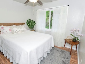 Quarto com uma cama, um vaso de plantas, uma pequena mesa com uma planta e uma janela com cortinas.