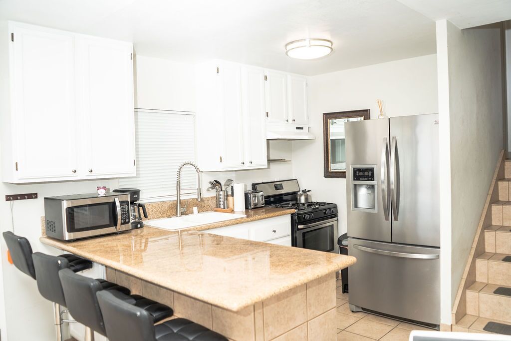 A modern kitchen with white cabinets, a stainless steel refrigerator, a microwave, and a gas stove.