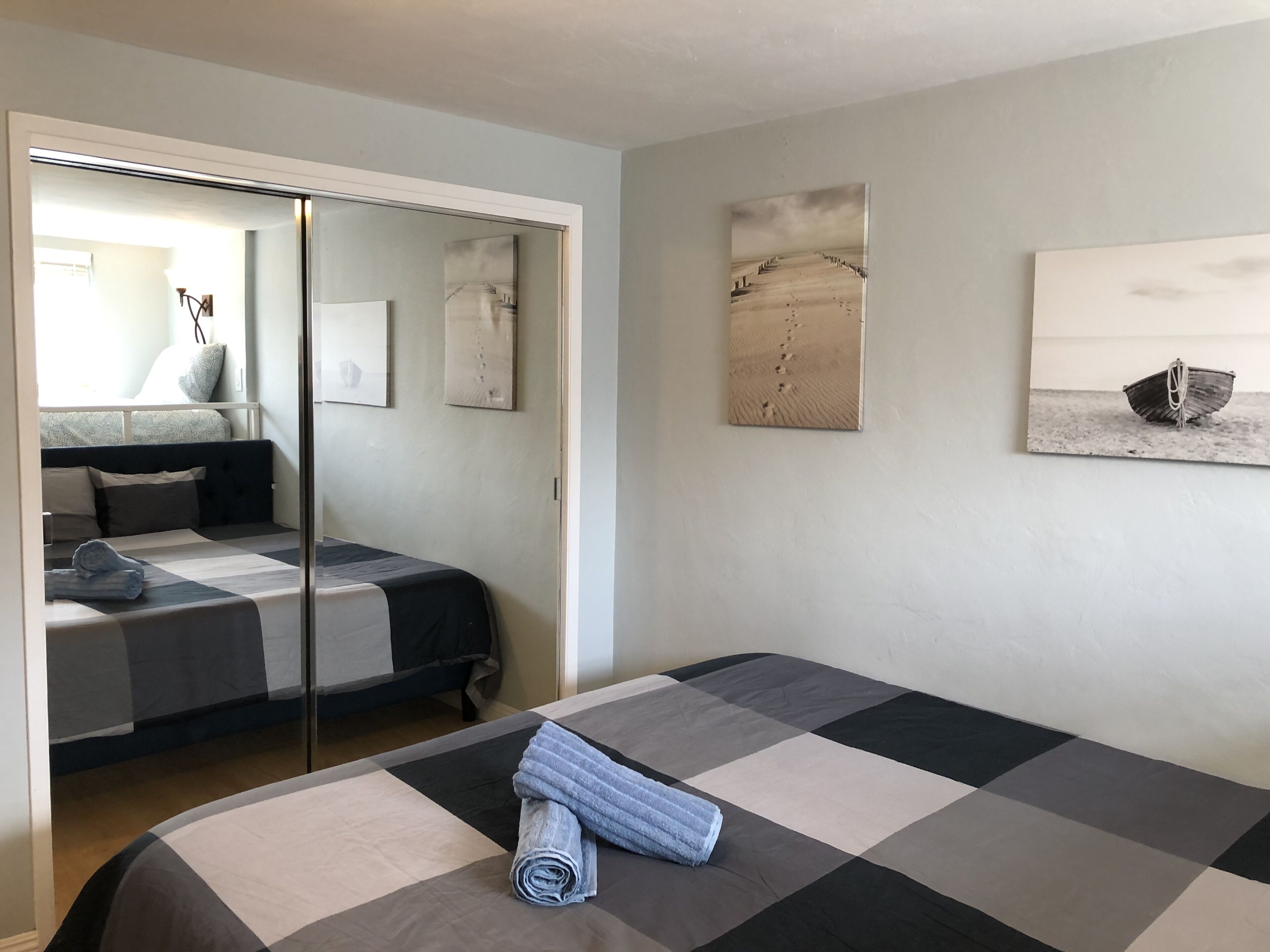 Ein Schlafzimmer mit karierter Bettdecke, einem Spiegel und Bildern an den Wänden.