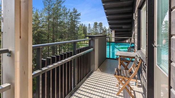 A wooden deck with a metal railing, a small table with chairs, and a view of a swimming pool and trees.