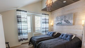A bedroom with two beds, a wooden floor, a black rug, a chandelier, and a wall-mounted painting.