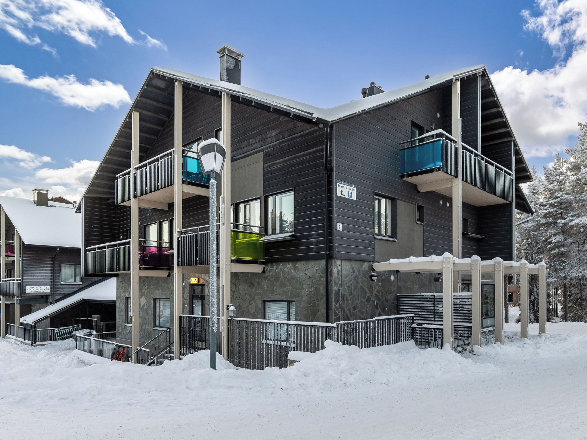 A multi-story building with balconies, a covered entrance, and a snow-covered ground.