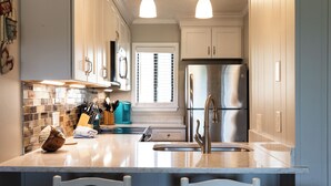 Une cuisine moderne avec des armoires blanches, un réfrigérateur en acier inoxydable et des luminaires suspendus.