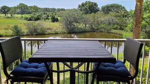 Une table et deux chaises sur un balcon donnant sur un étang bordé d’arbres et de verdure.