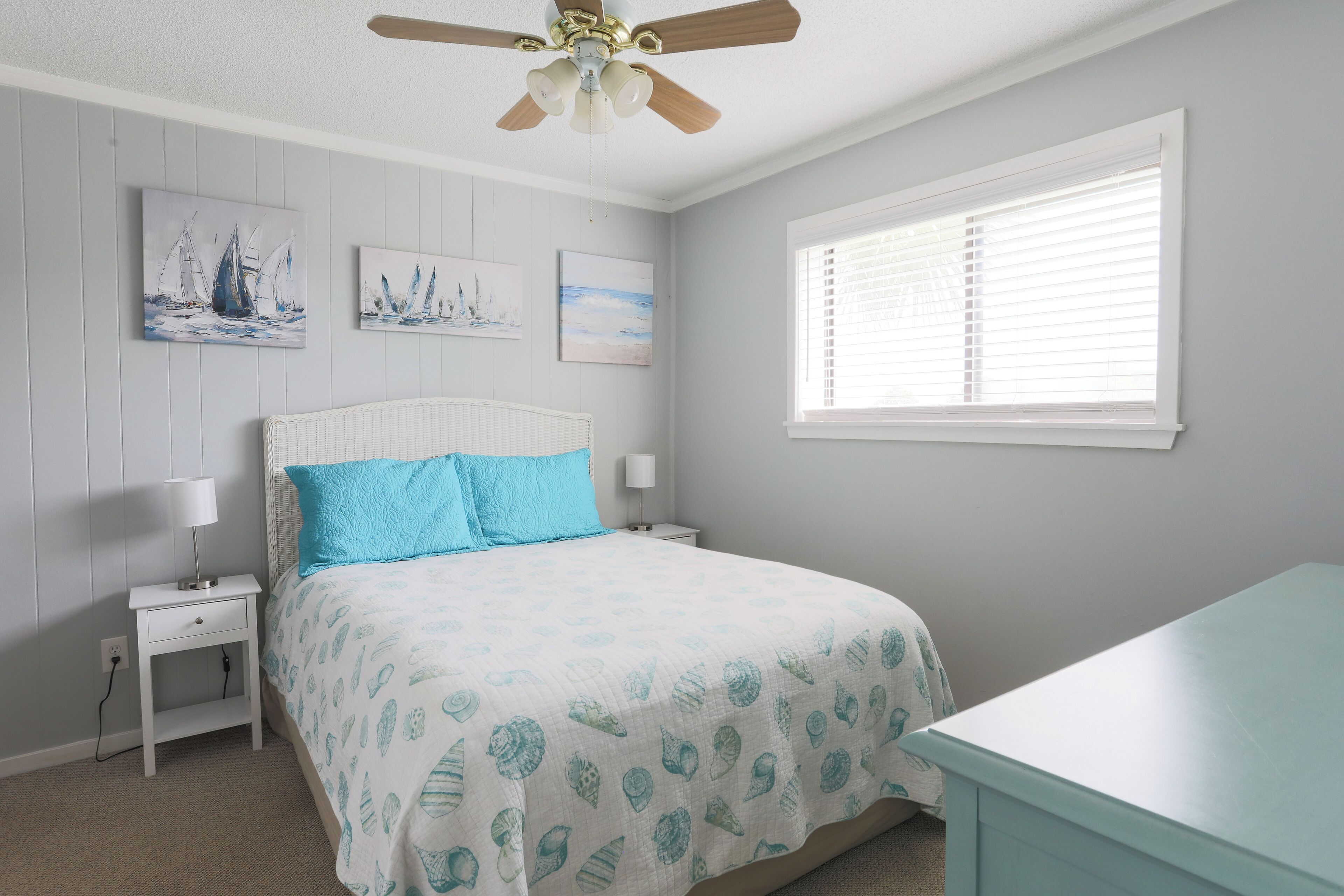 A bedroom with a bed, nightstands, a ceiling fan, and artwork on the wall.