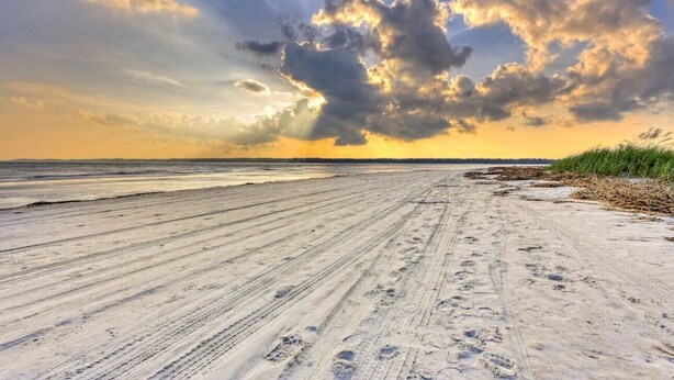 Une plage avec un large chemin de sable et des empreintes de pas qui mènent à l’eau.