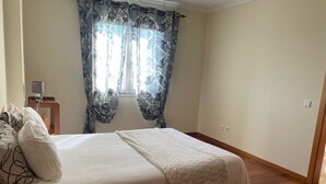 Une chambre à coucher avec un lit, des rideaux, une table de chevet avec une lampe et un plancher en bois.