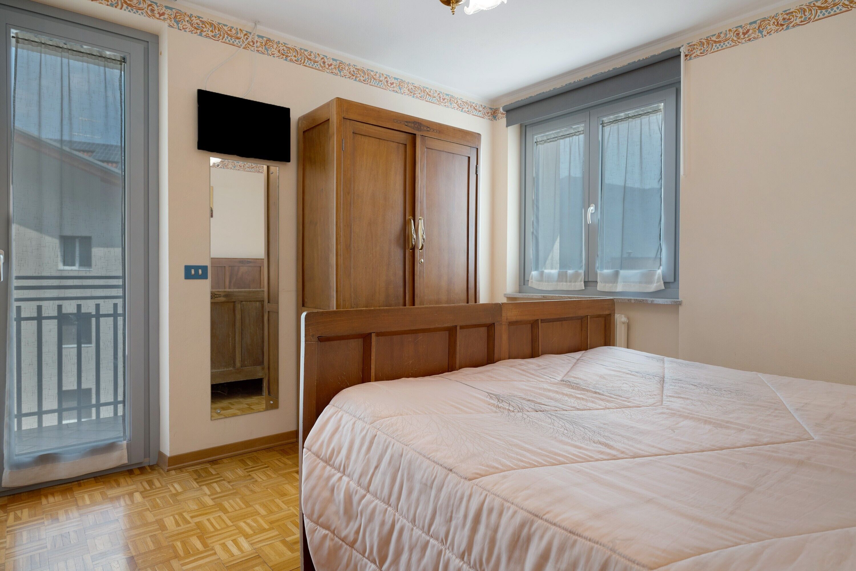 Un dormitorio con cama, armario, televisor y ventana con cortinas.