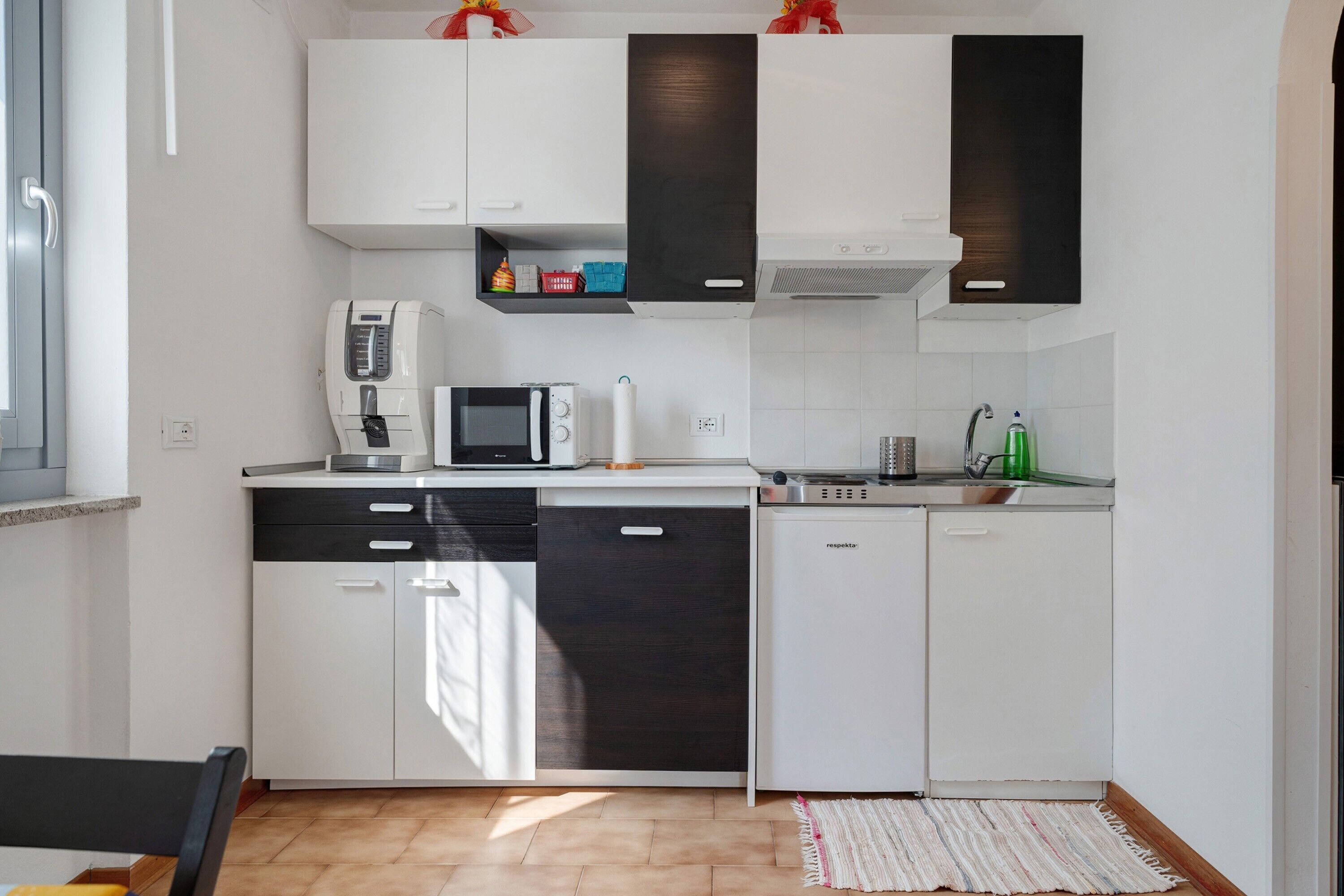 Una cocina moderna con armarios blancos y oscuros, microondas, cafetera y lavavajillas.