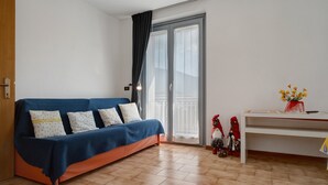 A room with a sofa, a small table, a vase with flowers, and a balcony door.
