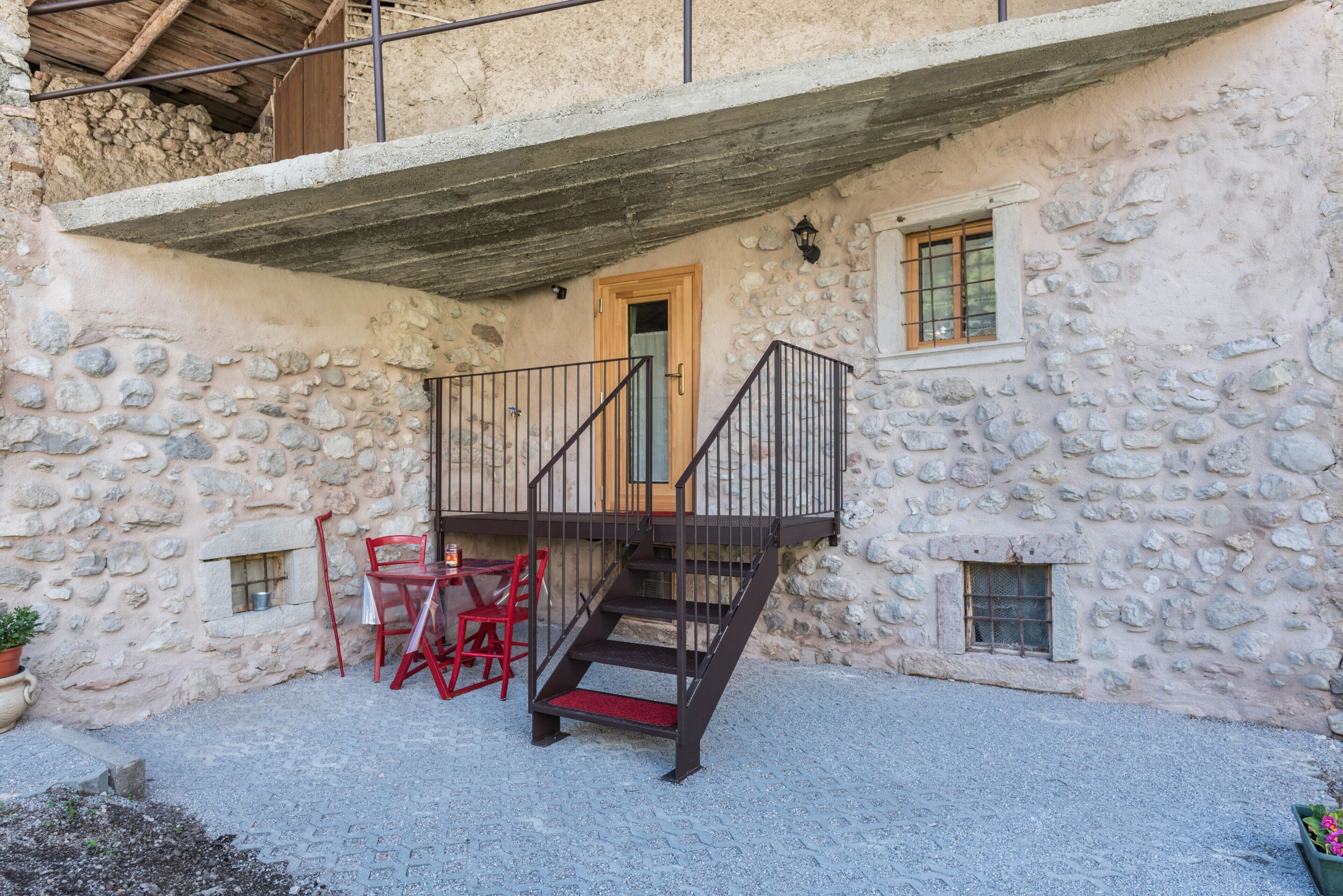 A stone building with a wooden door, a staircase with a metal railing, and a red chair outside.