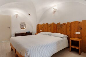 A bedroom with a wooden headboard, a bed with striped bedding, a nightstand, and a wall-mounted light fixture.