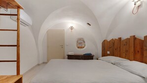 Een slaapkamer met een houten stapelbed, een enkel bed met gestreept beddengoed, een klein houten nachtkastje en een witte deur.