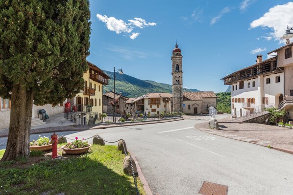 Una plaza de pueblo con una torre destacada, edificios tradicionales y un cielo despejado.