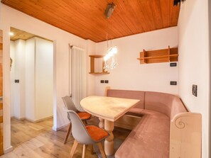 A modern interior with a wooden ceiling, a dining table with chairs, a sofa, and a radiator.
