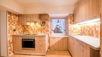 A compact kitchen with wooden cabinets, a built-in oven, and a window with curtains.