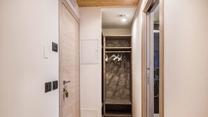 Ein schmaler Flur mit einer Holztür, einer weißen Wand mit Thermostat und einer Wand mit Muster und Kleiderhaken.