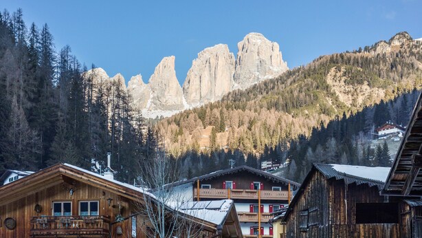 Ein Bergdorf mit Holzhäusern, einem Balkon und Blick auf schroffe Berggipfel.