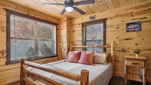 A log cabin bedroom with a bed, a bench, a small table, and a ceiling fan.