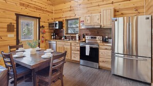 A wooden cabin kitchen with a dining table set for four, a stainless steel refrigerator, and wooden cabinets.