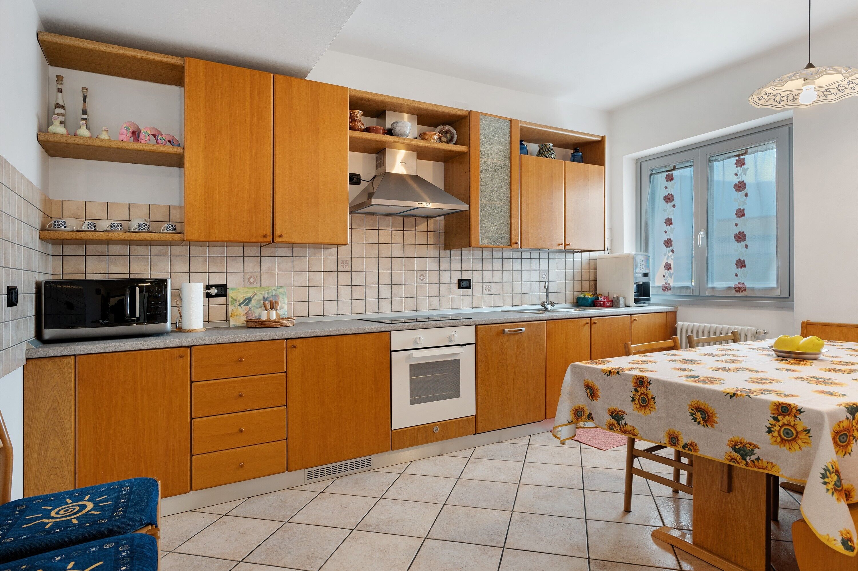 Una cocina con armarios de madera, un microondas, un horno y una mesa de comedor con mantel de girasoles.