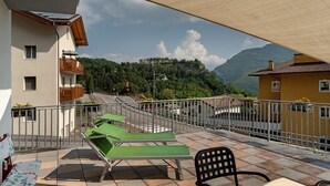 A balcony with green lounge chairs, a table, and a chair, overlooking a road and mountains.