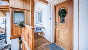 Ein Holzbalkon mit einem Stuhl, einer Tür mit einem Kranz und einem Fenster mit Vorhängen.