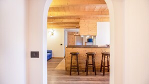 Eine Küche mit Holzausstattung, einer Bar mit Hockern und einem blauen Sofa im Hintergrund.