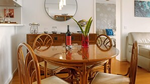 A dining area with a round wooden table, chairs, a mirror, and a vase with a plant. - Luzias Apartment with Sea View, Wi-Fi & Balcony (Funchal)