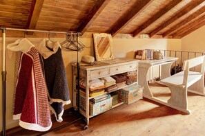 A rustic attic room with a wooden ceiling, a metal rack with towels, a dresser with drawers, and a small table.